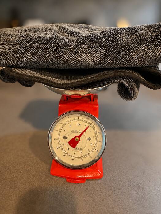 Competitor's microfiber towel on the same Fox Run scale — needle barely past zero, weighing in around 0.8 lb